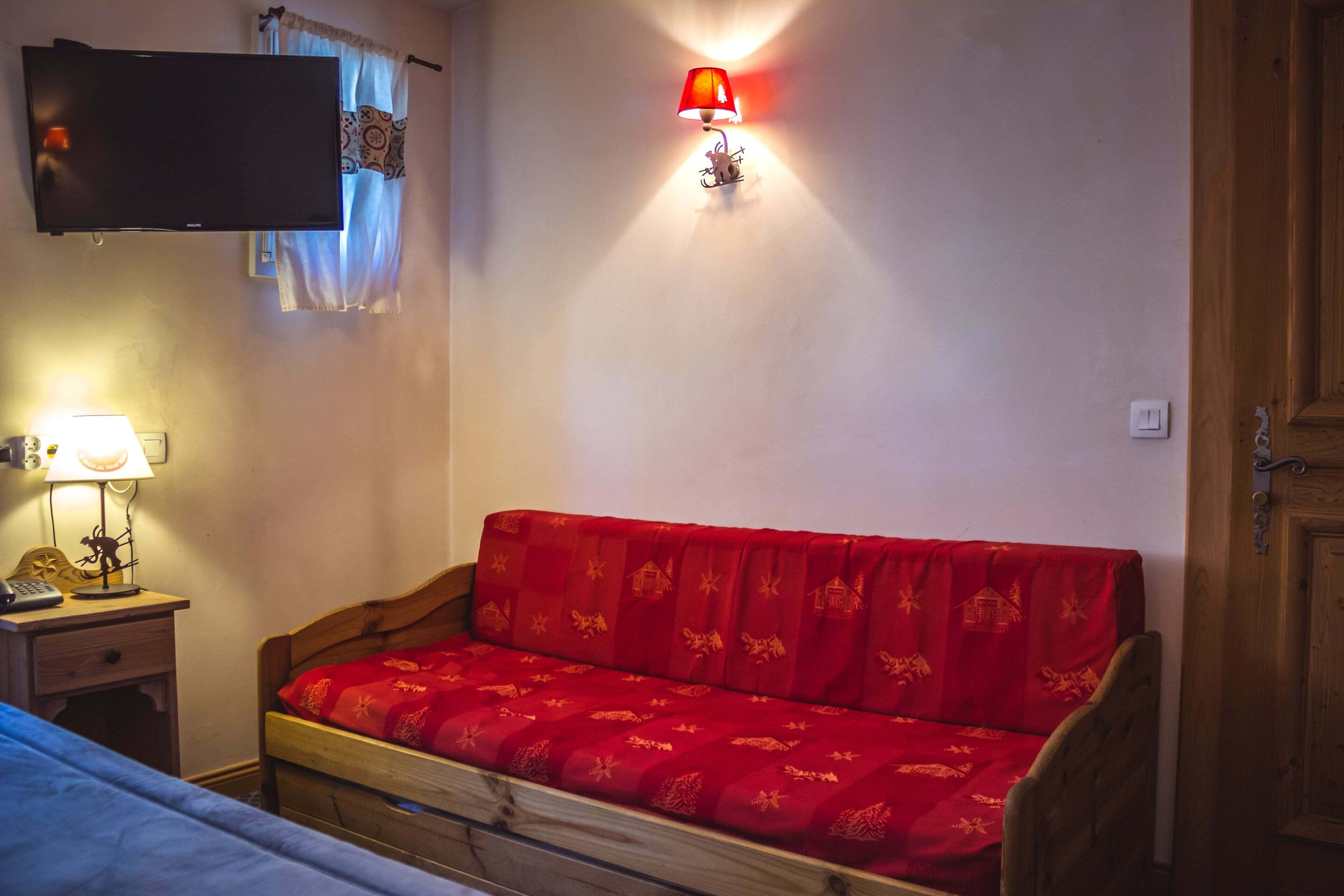 Een slaapkamer met een houten bed, een rode bank, een nachtkastje met een lamp, een televisie aan de muur en een wandlamp.