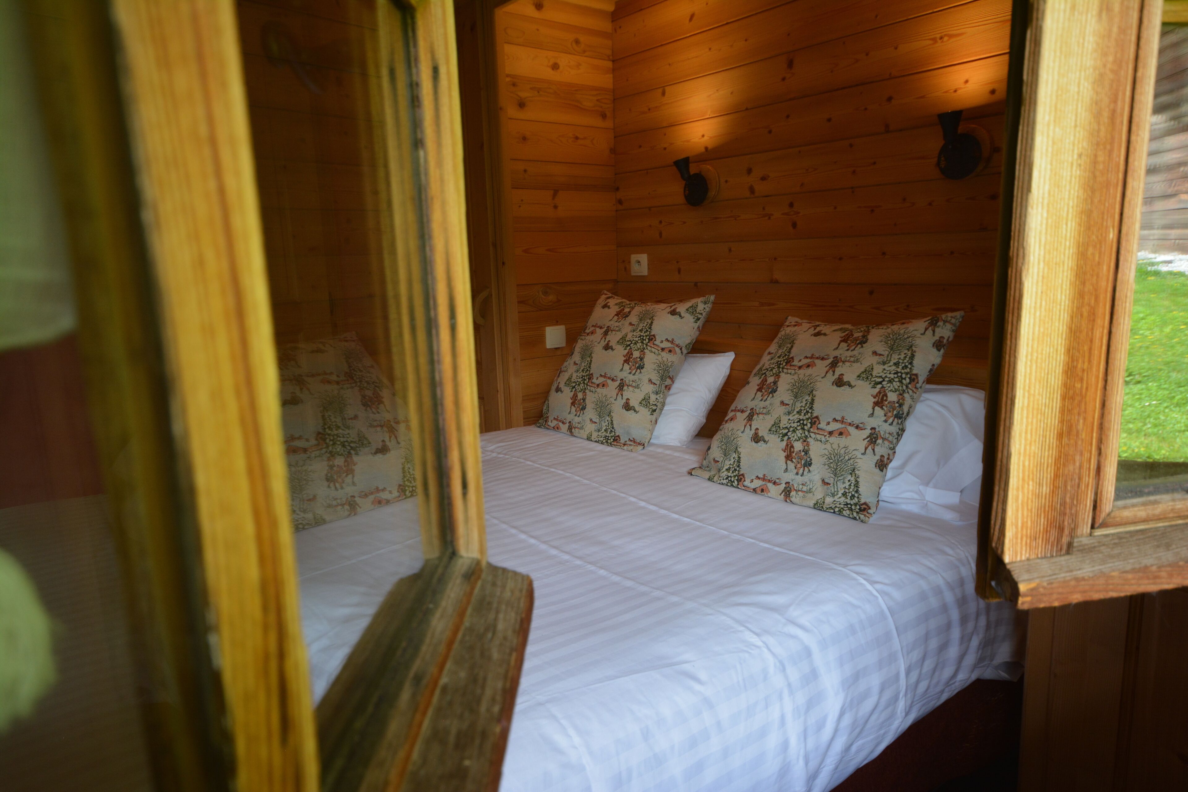 A wooden cabin room with a bed, floral pillows, and a window.