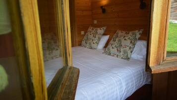 A wooden cabin room with a bed, floral pillows, and a window.