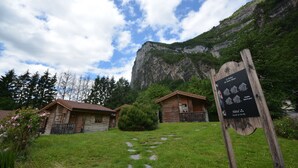 A wooden cabin with a mountain backdrop, a signboard with text, and a stone pathway. - Logis Hôtel le Relais du Mont Blanc (Magland)