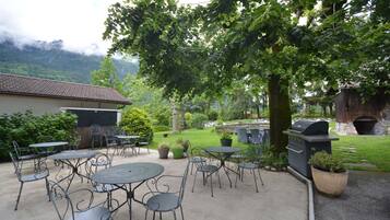 Une terrasse extérieure avec des tables et des chaises en métal, un barbecue et un four en pierre.