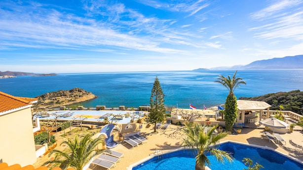 A resort with a pool, sun loungers, and a view of the sea.