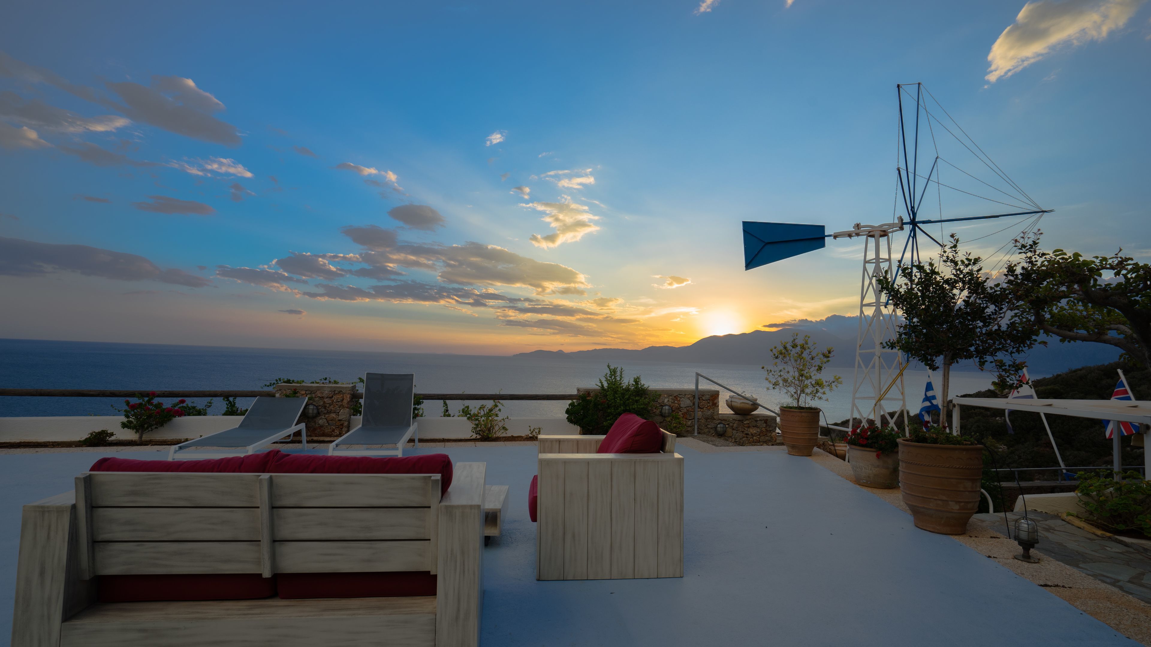 A terrace with lounge chairs and a view of the sea at sunset.
