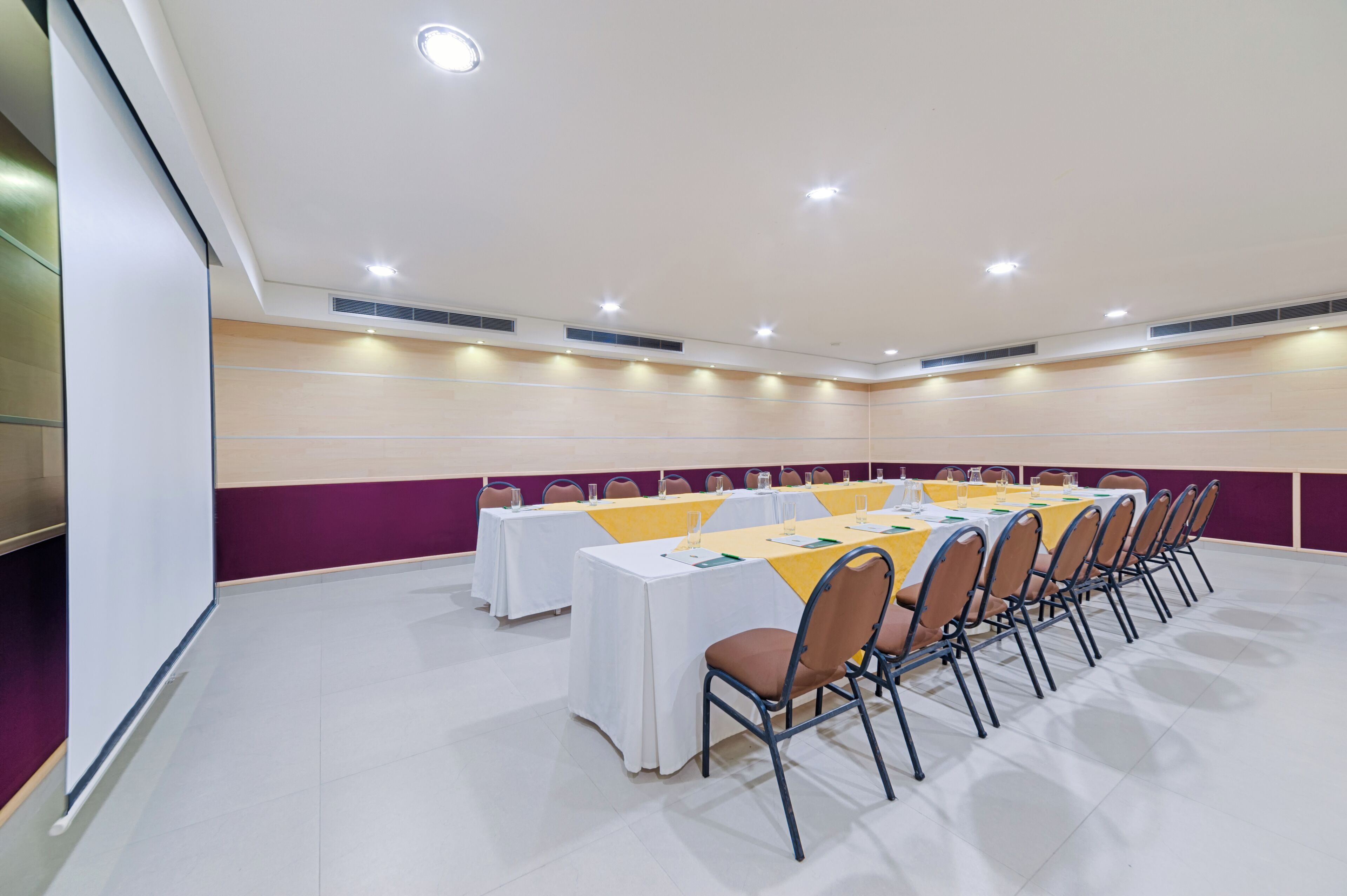 Ein Konferenzraum mit Tischen, Stühlen, weißen Wänden und Deckenleuchten.