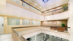 Un hall d’hôtel à plusieurs niveaux, doté d’un atrium en verre, de rampes en bois et d’un espace salon agrémenté de plantes.