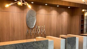 Un comptoir d’accueil avec un mur revêtu de panneaux en bois, une grande enseigne lumineuse indiquant « Hôtel Arizona Suites », et un luminaire moderne placé au-dessus.