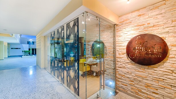 Un intérieur moderne avec une cloison en verre, un mur en pierre et une enseigne indiquant « Galeria Restaurante ».