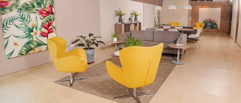 A modern lobby with yellow chairs, a gray sofa, and a dining area with yellow chairs.
