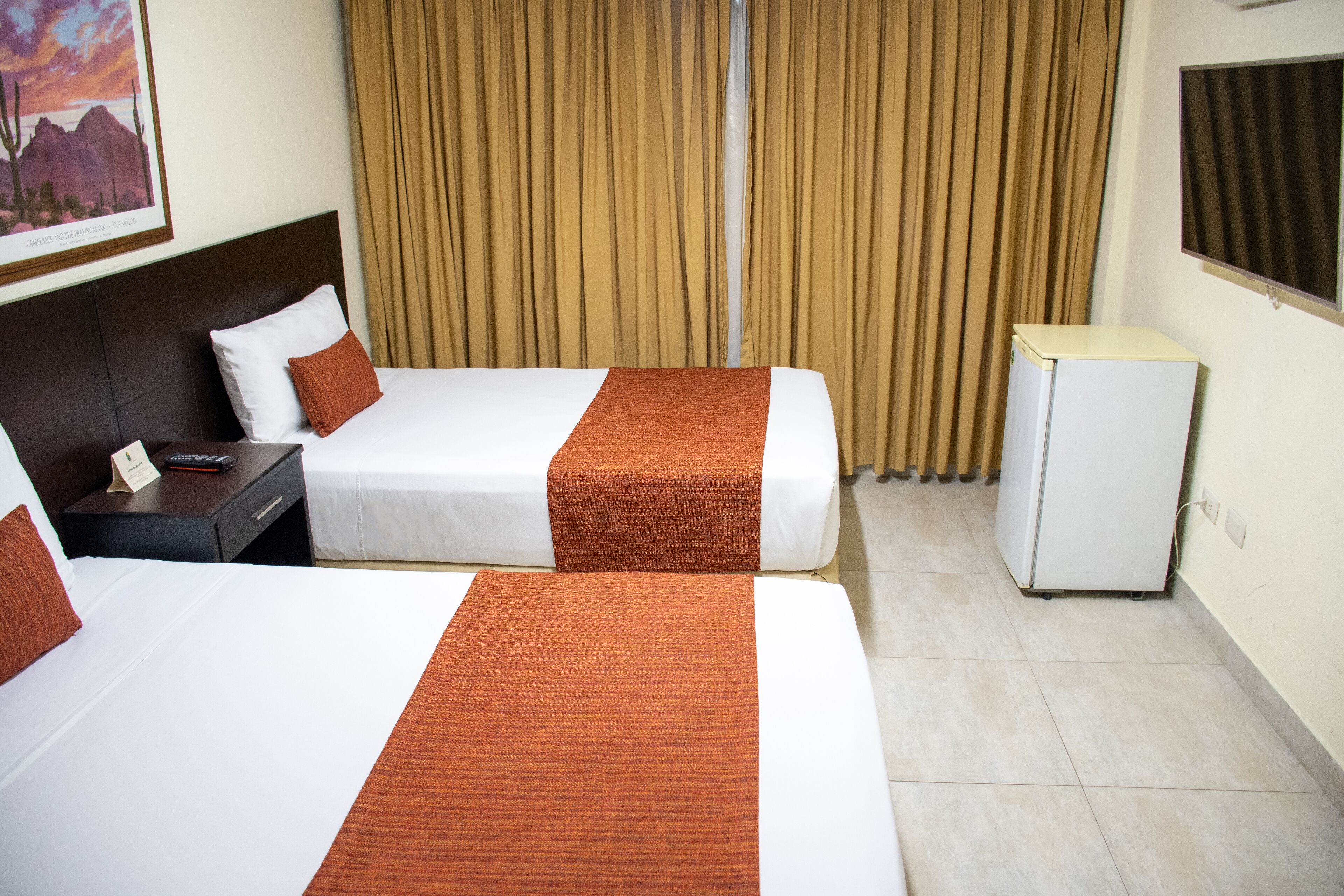 Habitación de hotel con dos camas, una mesita de noche, un refrigerador pequeño y una ventana con cortinas.