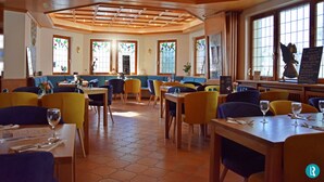 Een restaurant met zeshoekig betegelde vloeren, houten tafels en stoelen, en grote ramen met glas-in-lood.