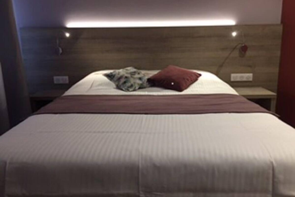 A neatly made bed with a white and brown bedspread, a single red pillow, and a patterned pillow.