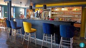 Een bar met een toonbank, krukken en planken vol flessen en glazen.