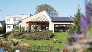 Een modern gebouw met een glazen gevel, een overdekt terras en een vijver met zwanen.