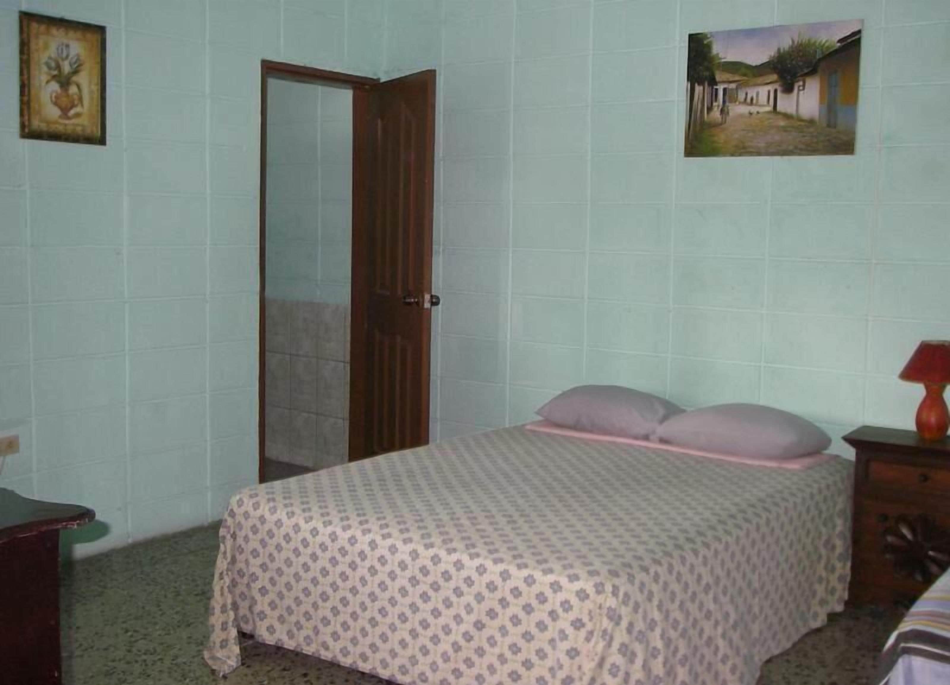 A bedroom with a bed, a wooden door, a small table, and a wall-mounted picture.
