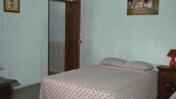 A bedroom with a bed, a wooden door, a small table, and a wall-mounted picture.