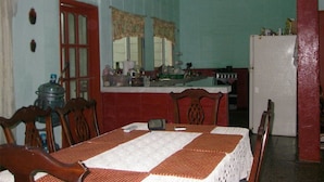 A dining area with a table set for two, a kitchen area with a refrigerator, and a window with curtains.