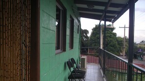 A balcony with two chairs, a green wall, and a view of the street.