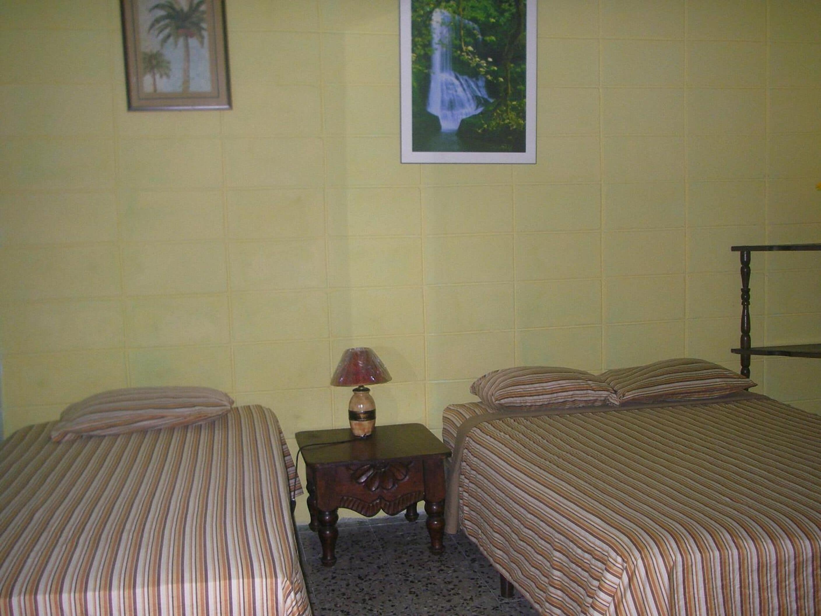 Una habitación con dos camas, una mesita de noche, una lámpara y dos cuadros en la pared.