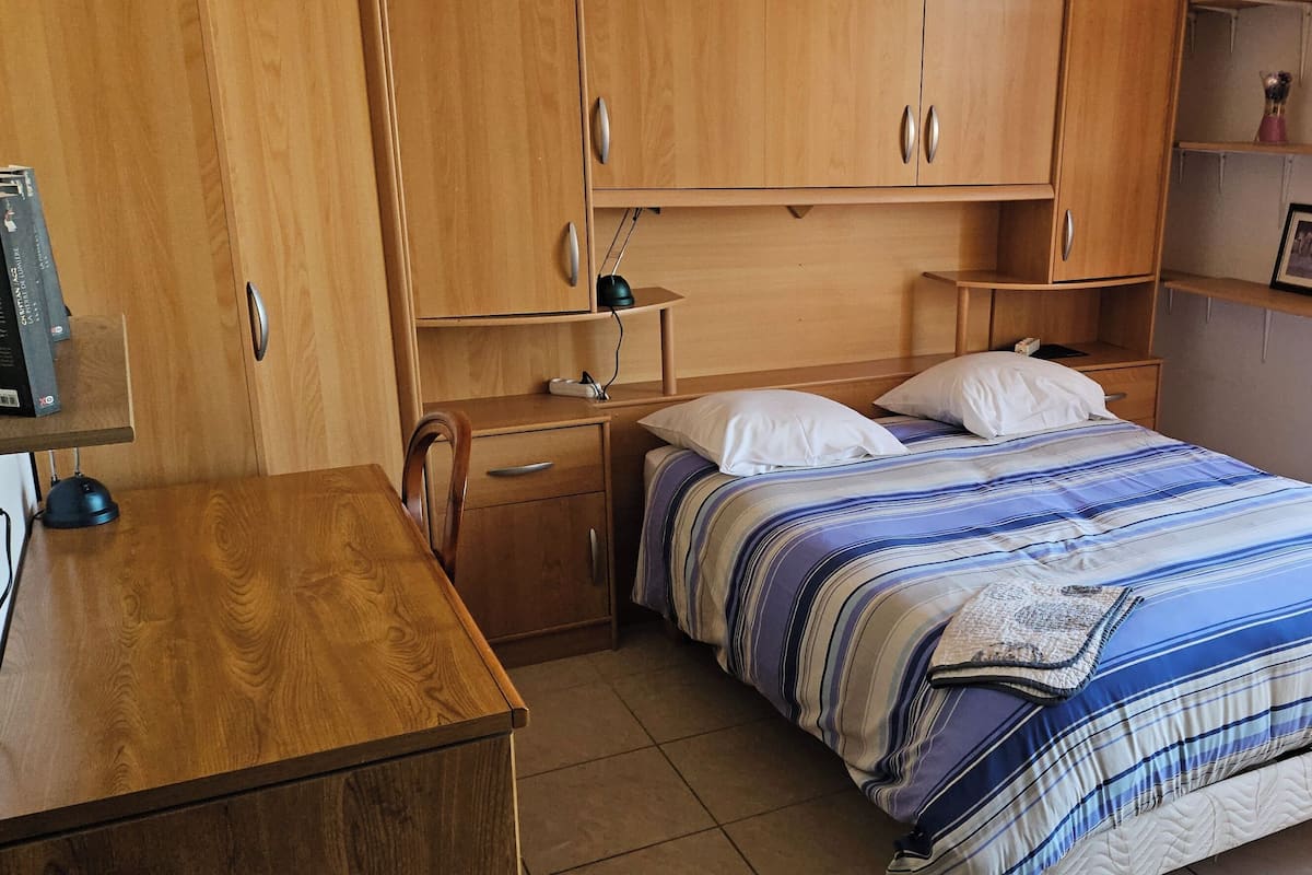 Un dormitorio con cama, armario de madera, mesita de noche y escritorio.