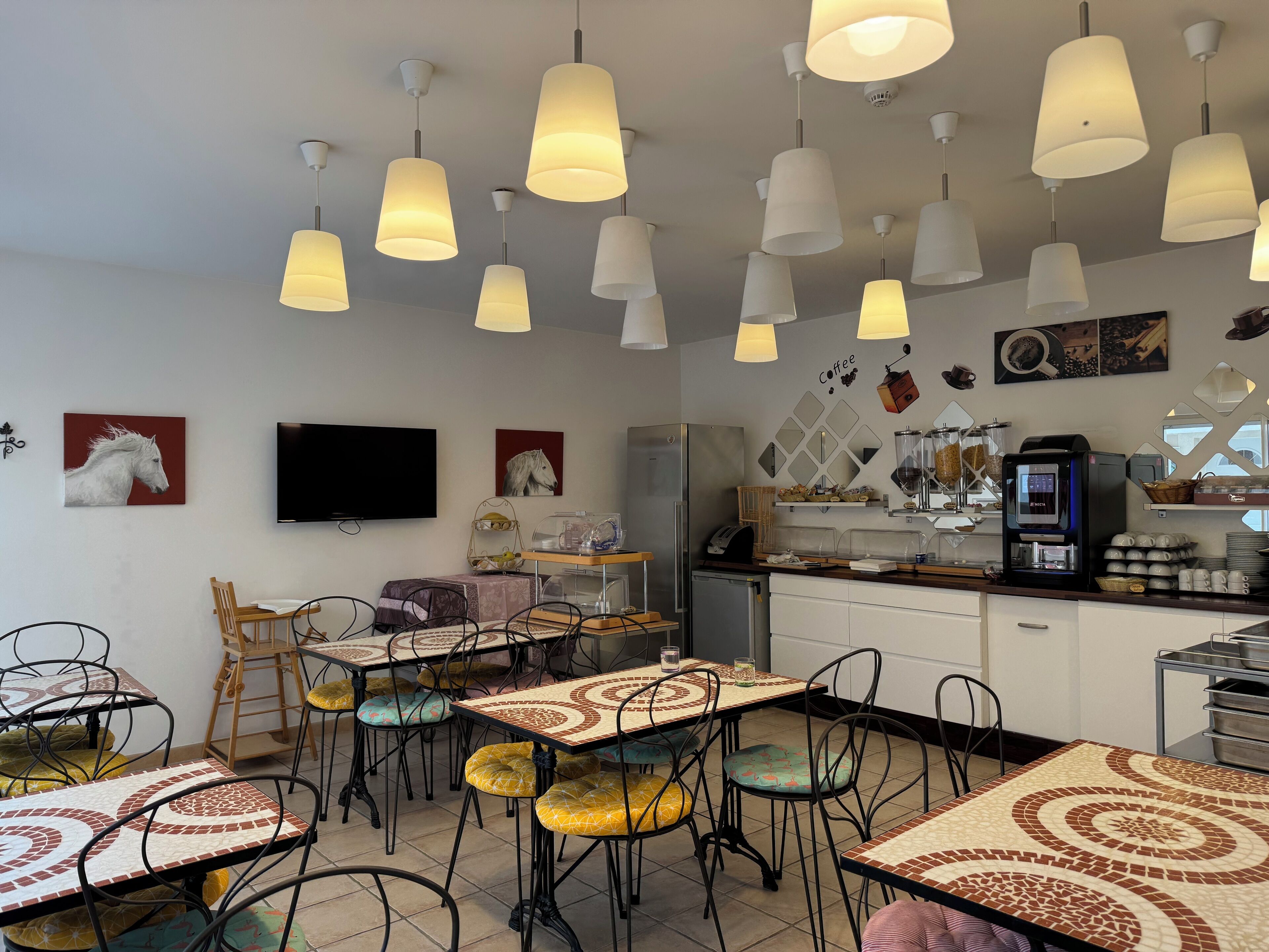 Un café con varias mesas y sillas, una máquina de café y un televisor en la pared.