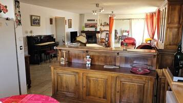 A cozy living room with a piano, a wooden cabinet, and a dining area with a red tablecloth.