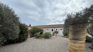 A courtyard with a gravel ground, surrounded by dense shrubbery and a stone pillar.