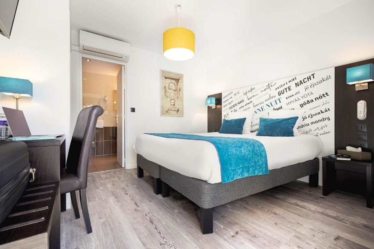 A modern hotel room with a bed, desk, chair, and a wall with text.