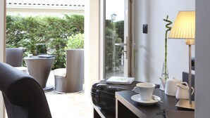 A room with a view of greenery, a table with a lamp, a chair, and a suitcase. - Contact Hôtels Les Pierres Dorées (Amberieux)