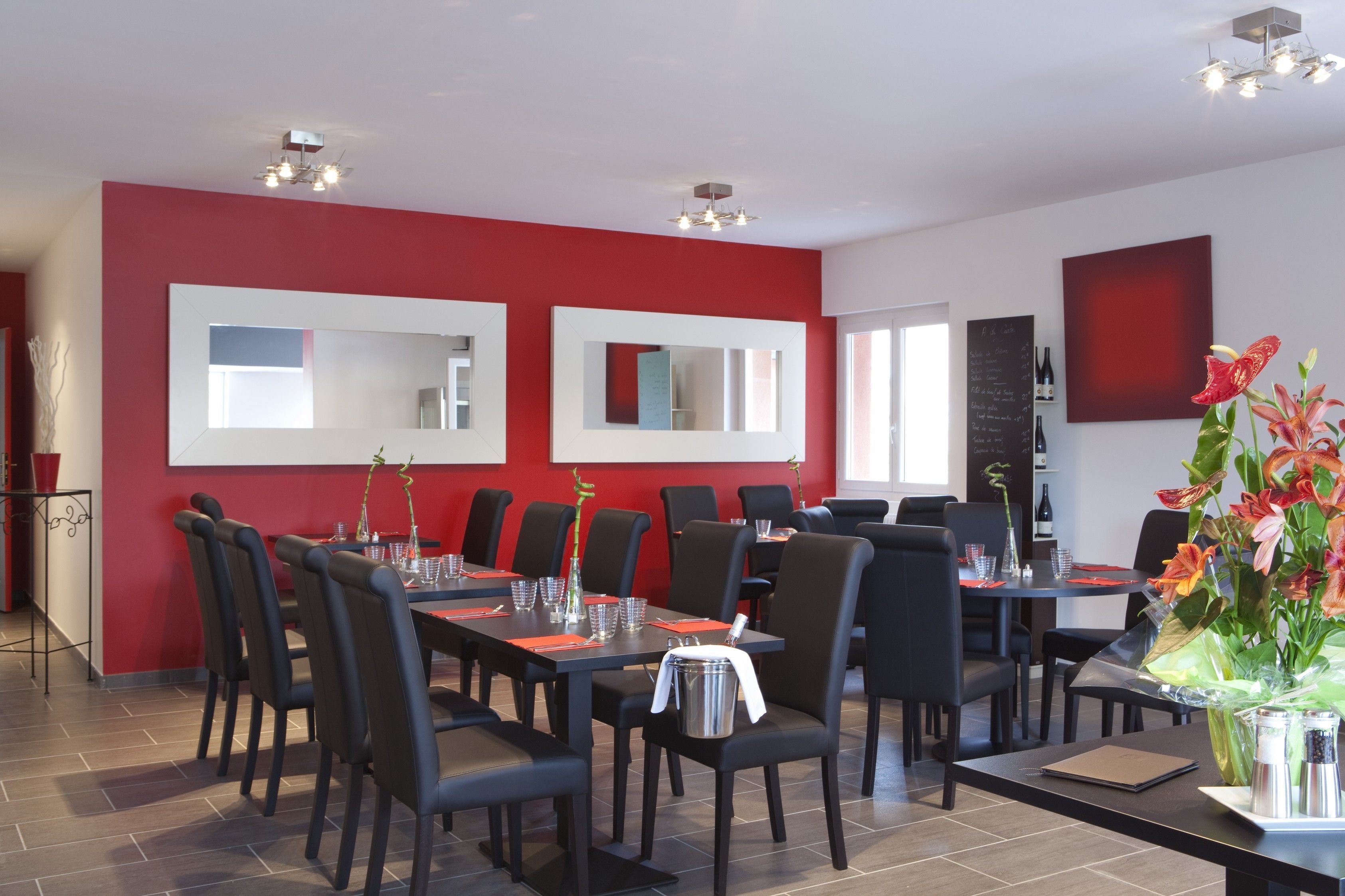 A dining area with red walls, multiple tables, black chairs, and modern lighting fixtures.