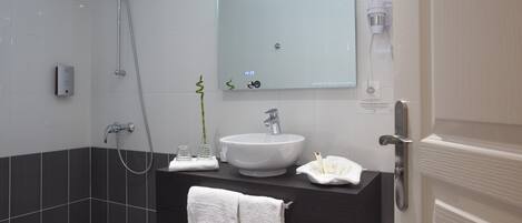 A modern bathroom with a white sink, dark tiles, a large mirror, and a shower.