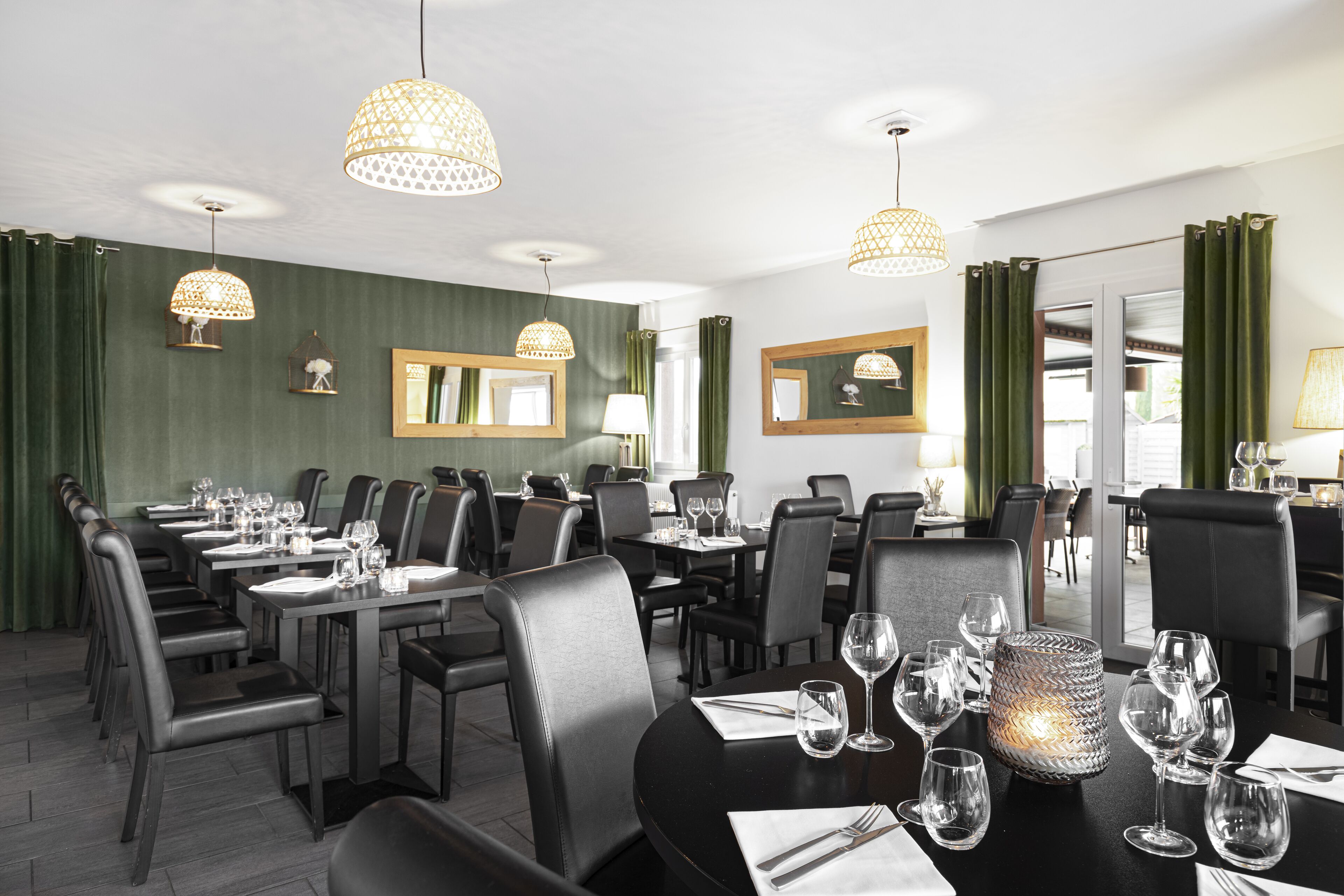 Un espace repas avec plusieurs tables dressées pour les convives, agrémenté de chaises noires et d’un lustre moderne.