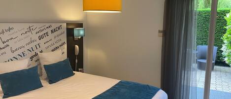A bedroom with a bed, a bedside lamp, a wall with text, and a view through a glass door.