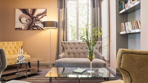 A modern living room with a sofa, a glass coffee table, a bookshelf, and a painting on the wall. - Contact Hôtels Les Pierres Dorées (Amberieux)