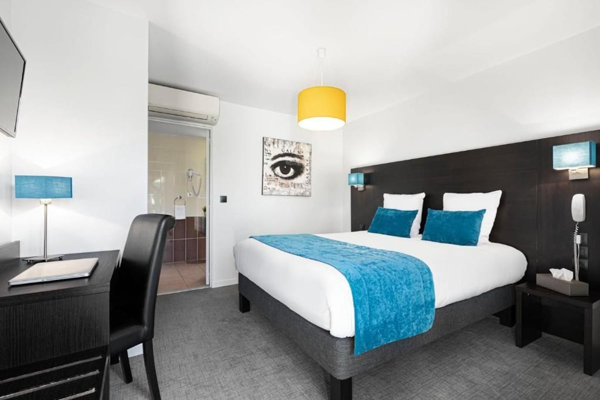 Habitación de hotel con cama, mesita de noche, lámpara y un cuadro en la pared.