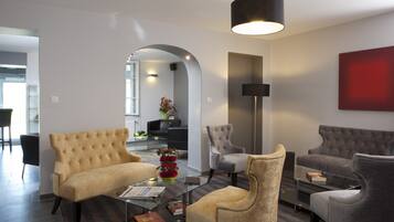 A modern living room with a sofa, armchairs, and a coffee table. There is a large mirror, a floor lamp, and a red artwork on the wall.