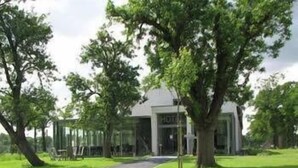 A modern building with a glass facade, surrounded by lush greenery and trees. - Cleythil Hotel (Maldegem)