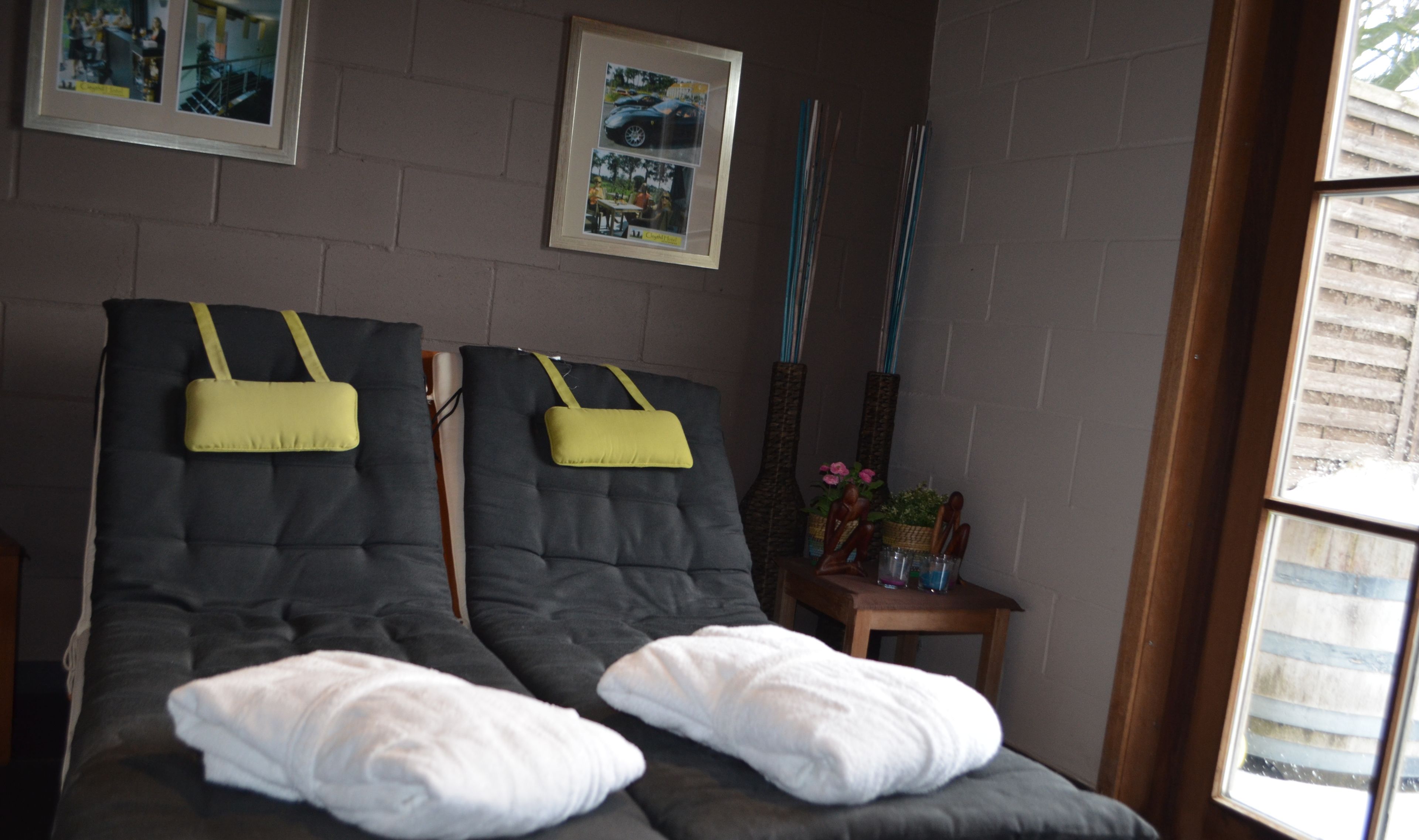 Um quarto com duas cadeiras de massagem, uma mesinha com um vaso e utensílios, e quadros nas paredes.