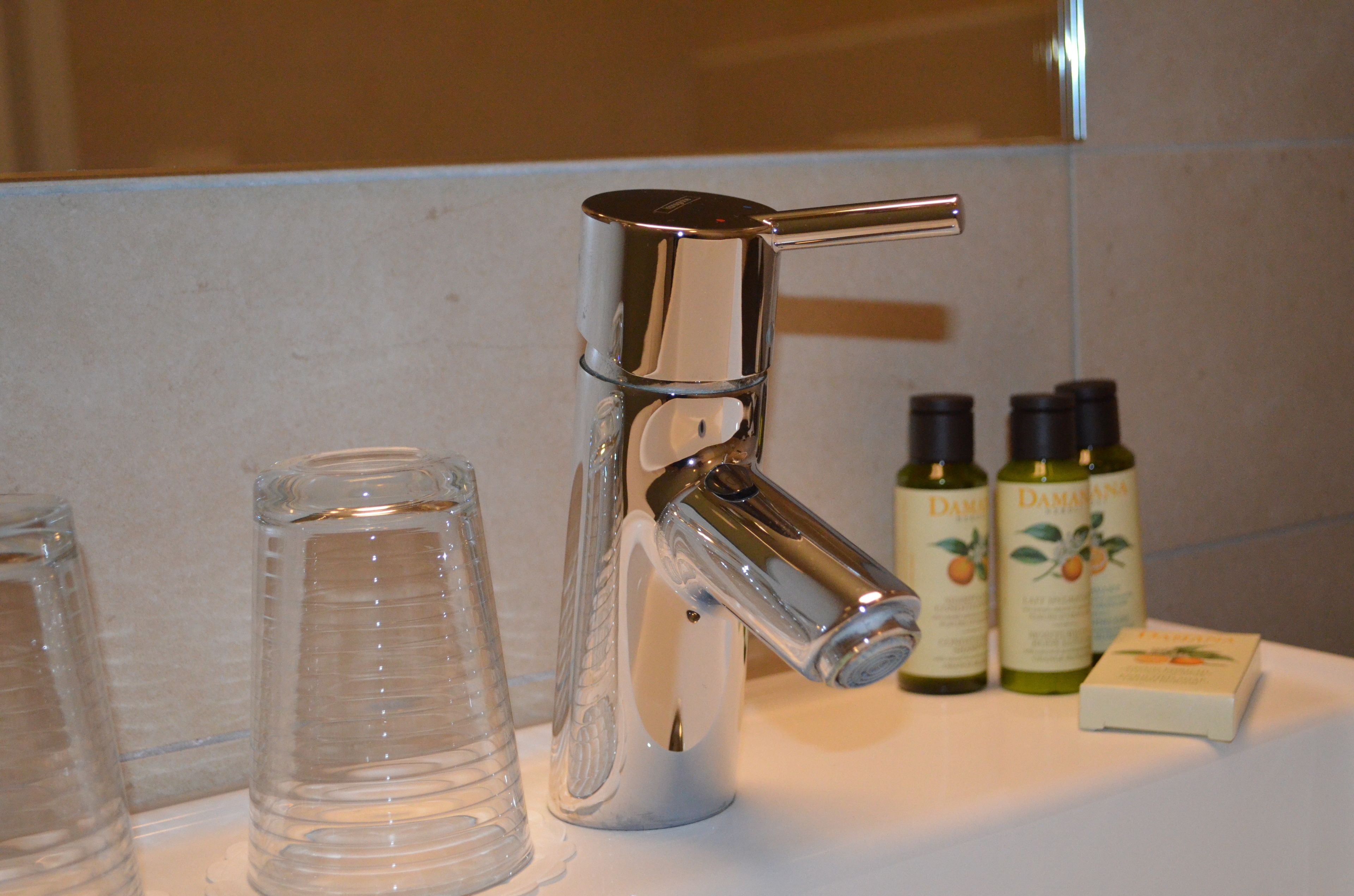 A bathroom sink with a chrome faucet, two glass containers, and two bottles of Damiana essential oil.