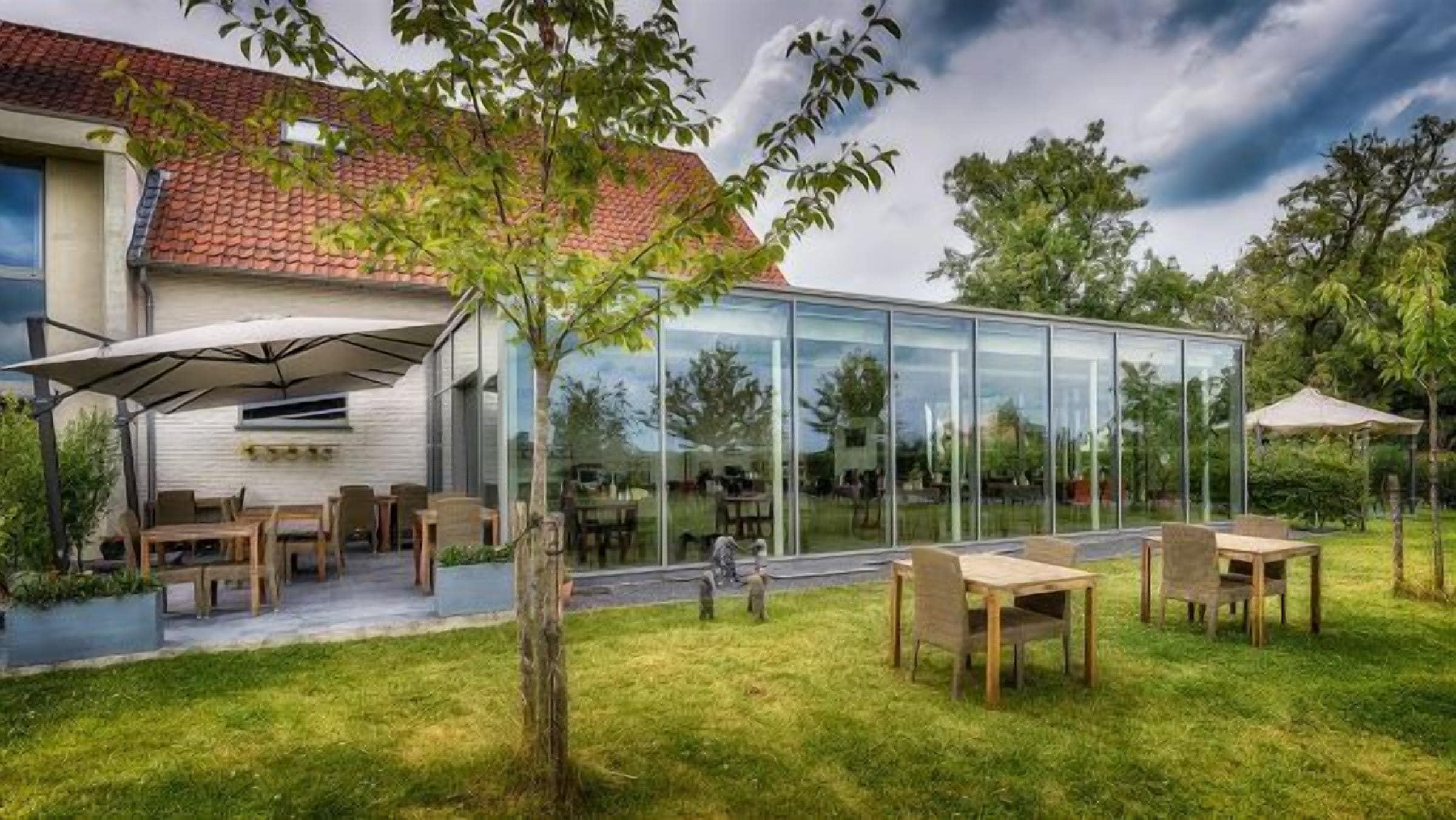 Une maison moderne dotée d’une véranda en verre, d’un espace salon extérieur et d’une pelouse bien entretenue.