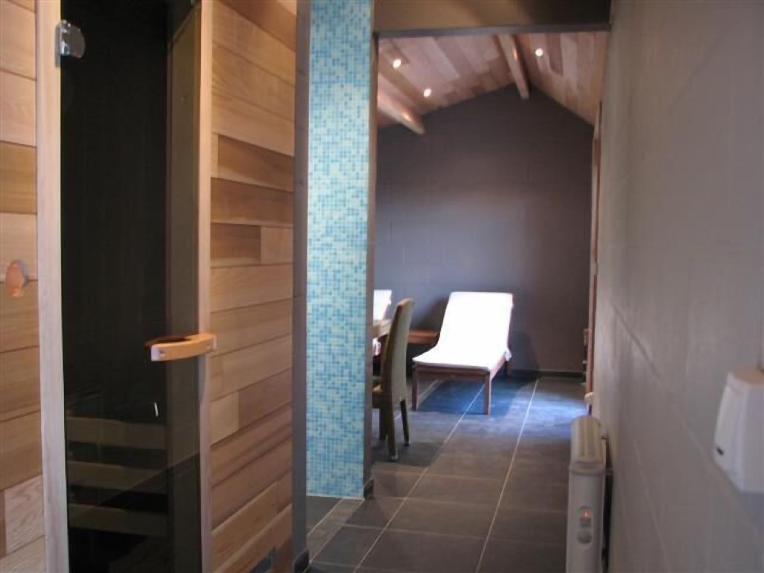 A hallway with wooden walls and a tiled floor, leading to a room with a bed and a chair.