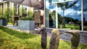 A modern building with a large glass facade, outdoor seating area, and a prominent umbrella structure. - Cleythil Hotel (Maldegem)