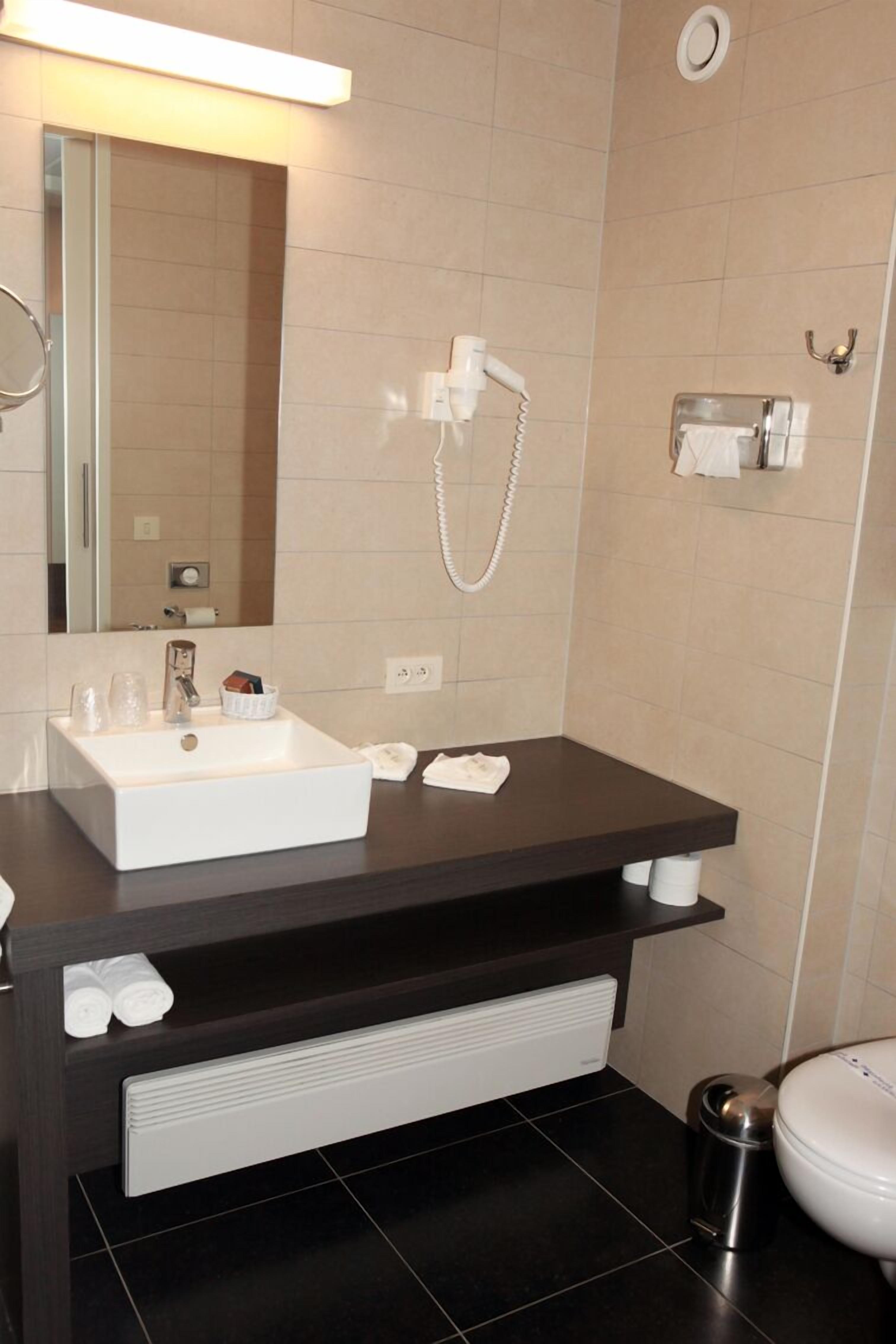 Un bagno moderno con lavandino bianco, piano di appoggio scuro e uno specchio.