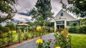 A modern hotel with a clear pathway leading to the entrance, surrounded by lush greenery and yellow flowers. - Cleythil Hotel (Maldegem)