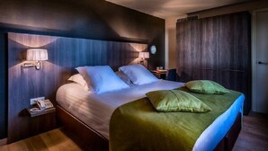 A hotel room with a large bed, two bedside lamps, a clock, and a wooden wardrobe. - Cleythil Hotel (Maldegem)
