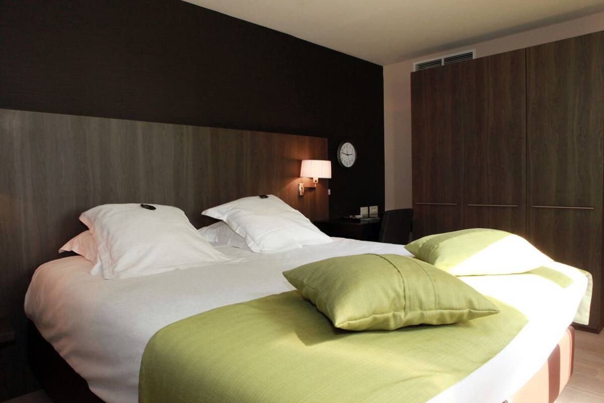 Habitación de hotel con una cama grande, una lámpara de noche, un reloj en la pared y un armario.