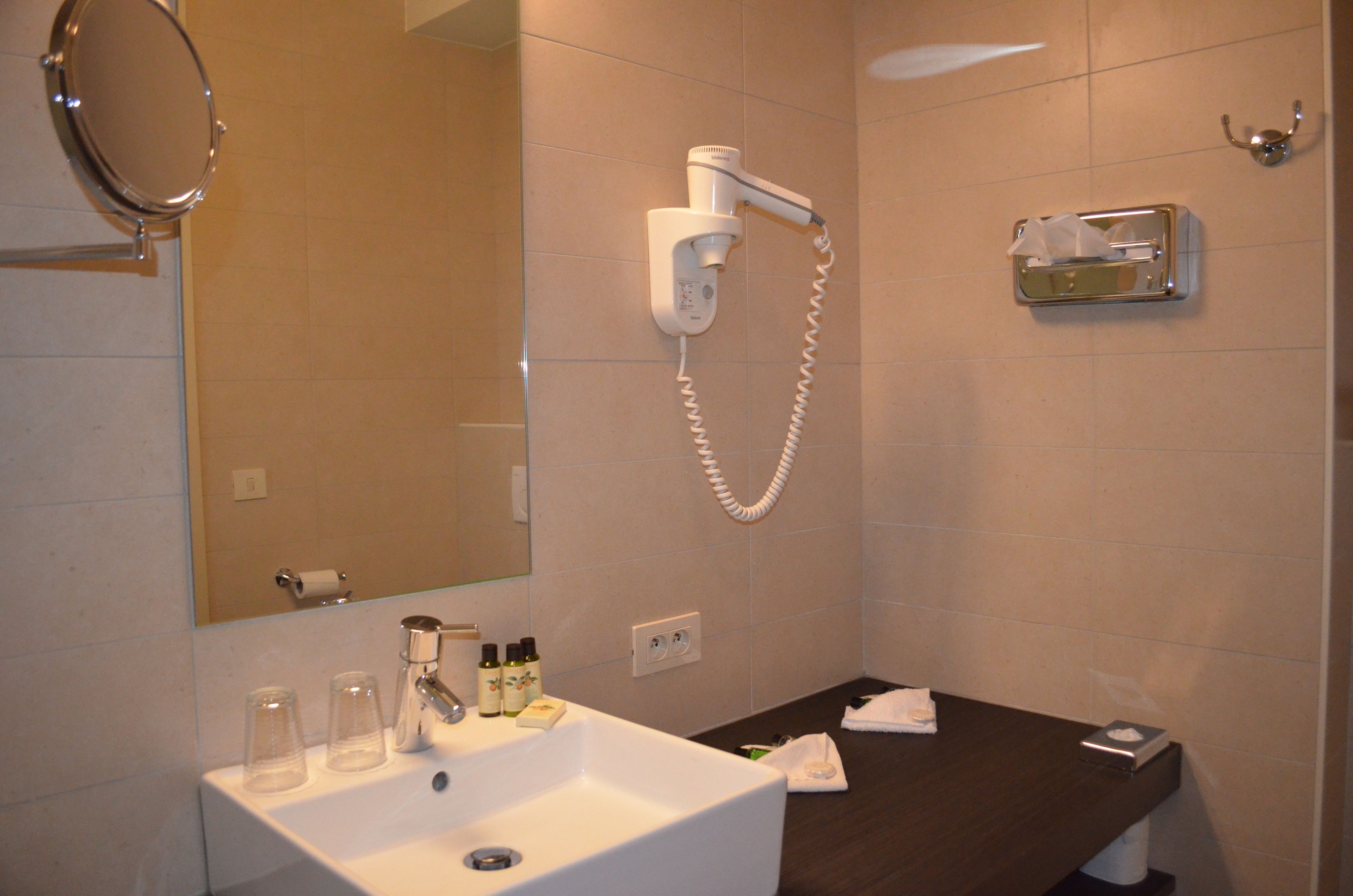 Un baño con lavamanos, espejo, secador de pelo y dispensador de toallas.