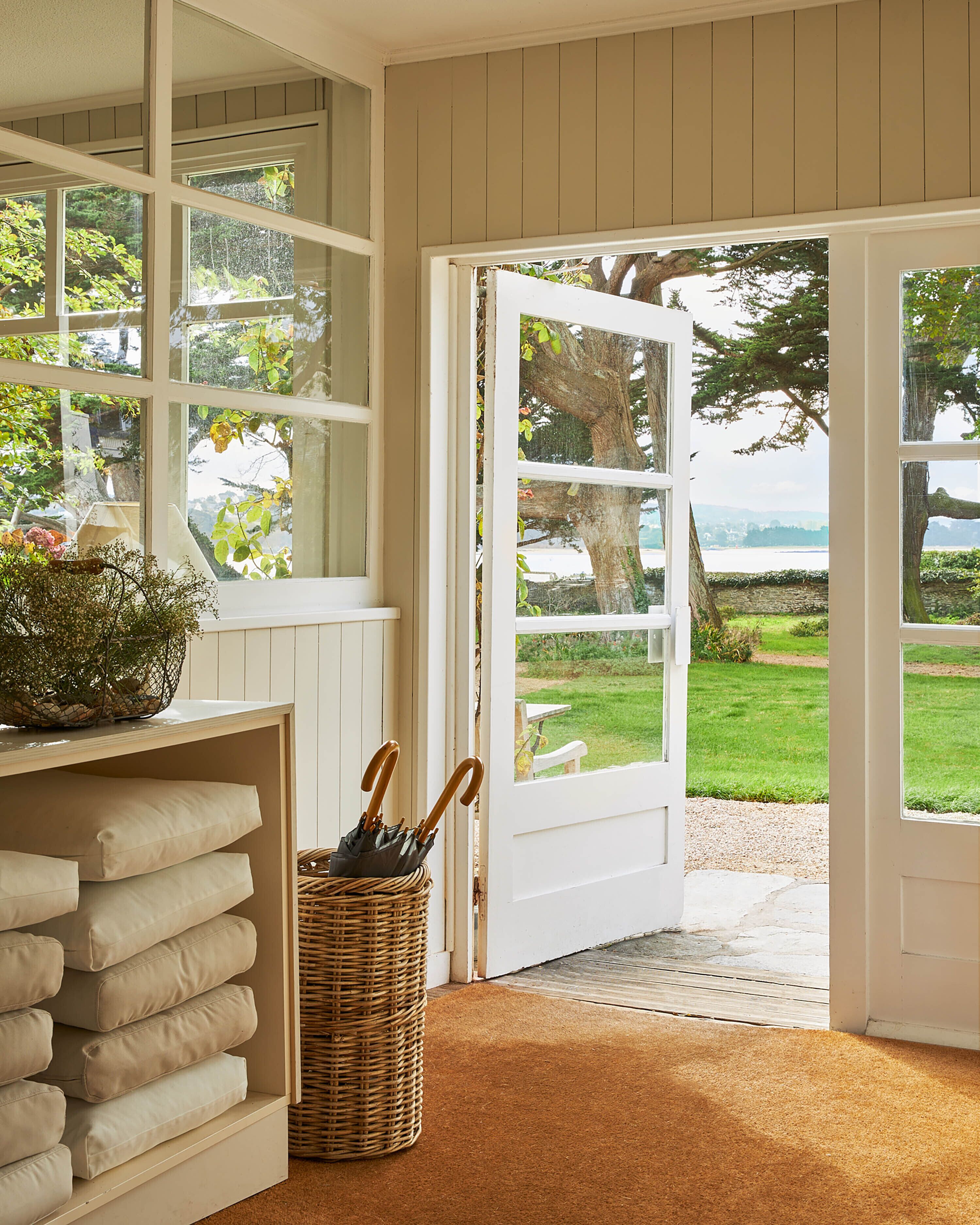 A room with a view of a grassy area and a body of water through large windows and an open door.