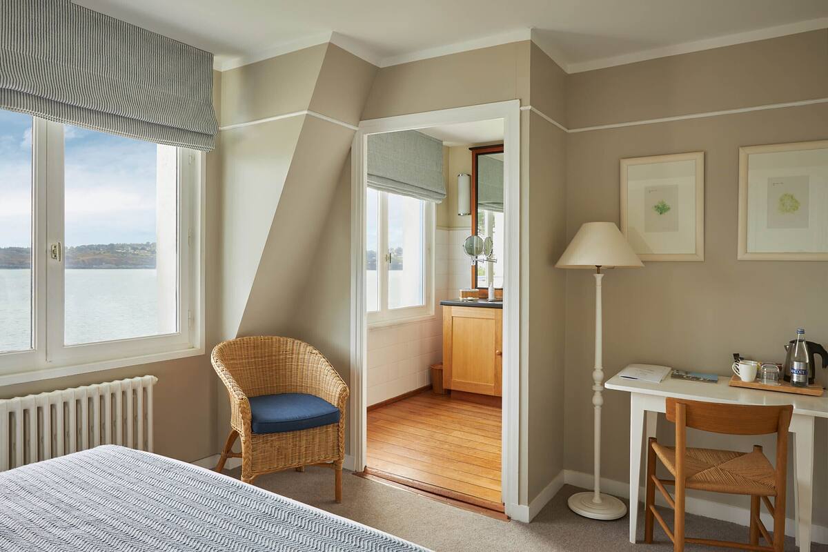 A bedroom with a bed, a chair, a desk, and a view of a lake.