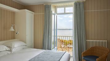 A hotel room with a large bed, a wicker chair, and a balcony with a view of the sea.