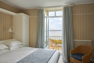 Habitación de hotel con una cama grande, una silla de mimbre y un balcón con vista al mar.